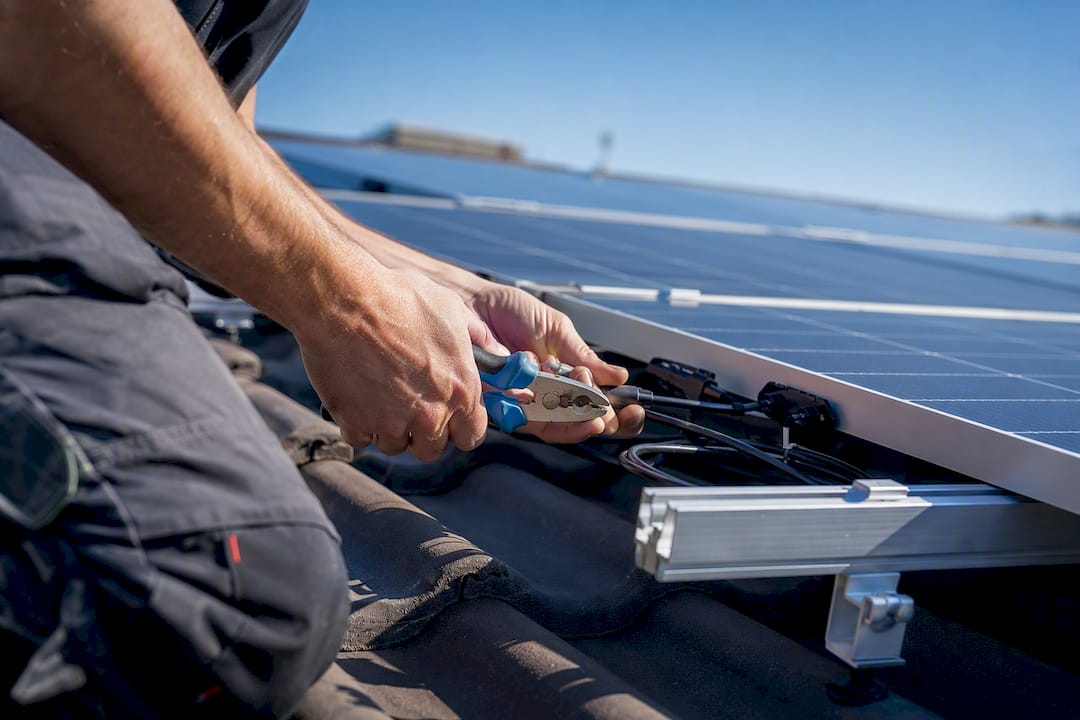 Hände verbinden Kabel an einer Solaranlage auf dem Dach