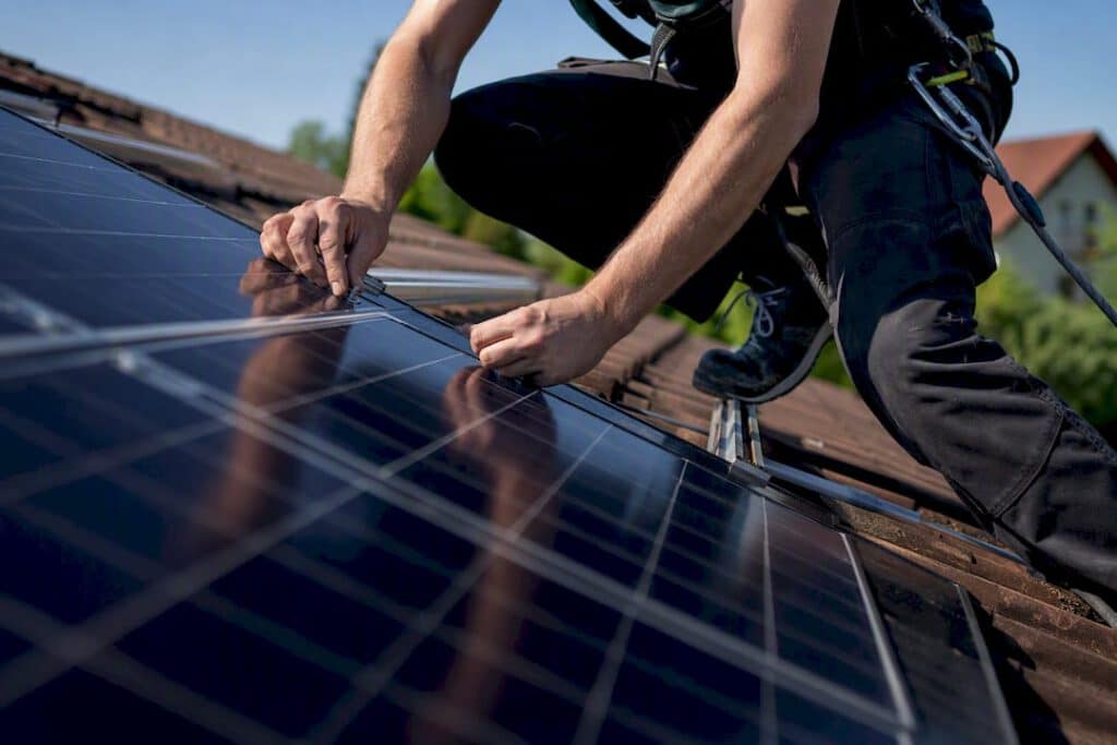 Ein Elektriker montiert Solarpanels auf dem Dach eines Hauses.