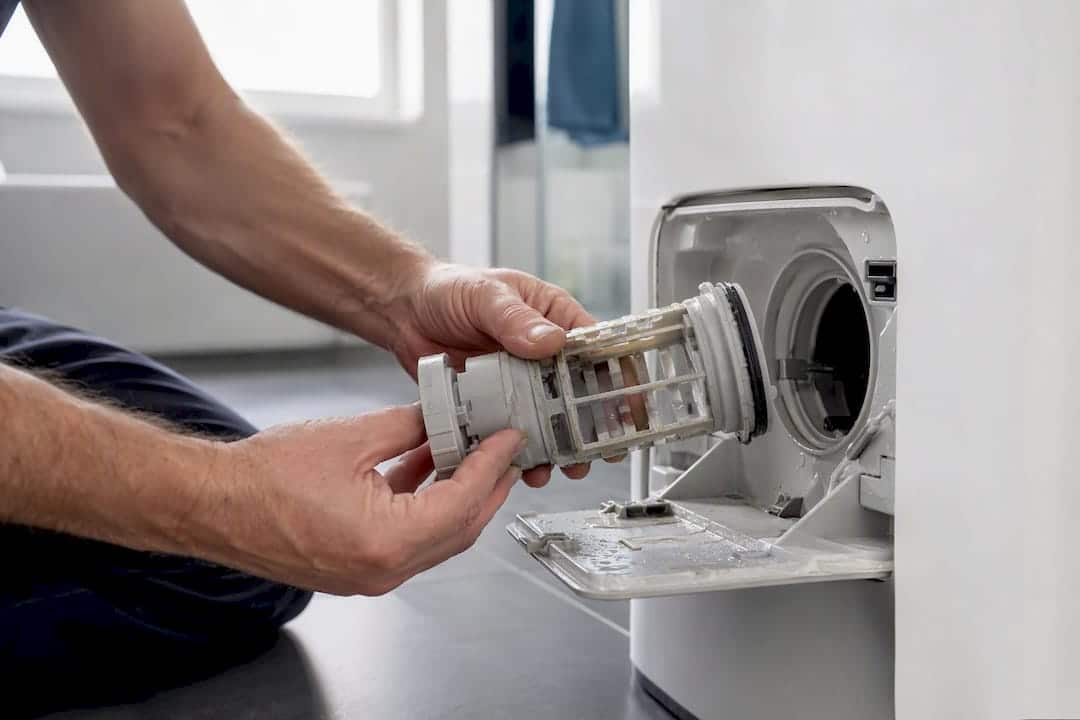 Haushaltsgeräte-Reparatur: Sofortmaßnahmen, Kosten und Ihr Recht 1 Mit den Händen wird das Flusensieb der Waschmaschine gereinigt.