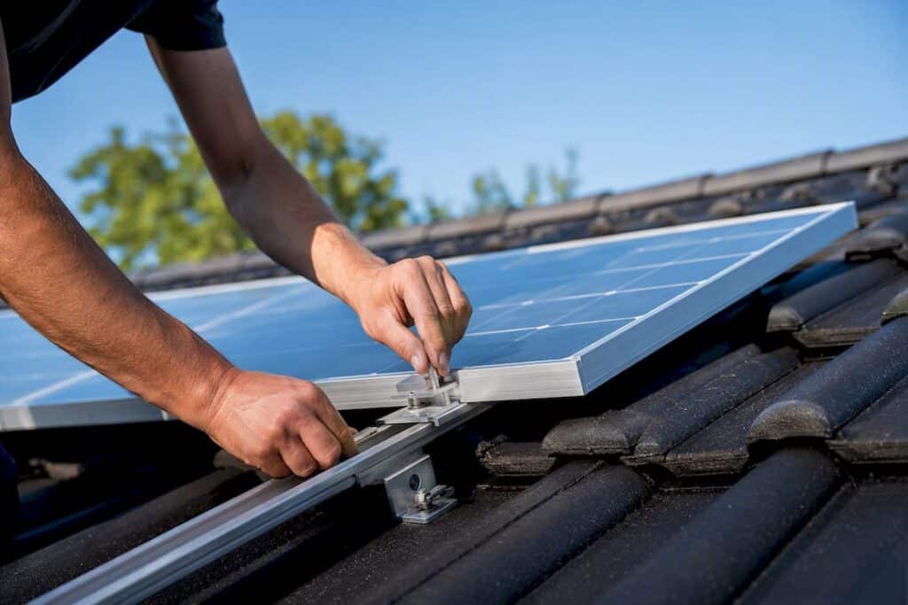 Hände, die eine Halterung für Solarpanels auf dem Dach anbringen